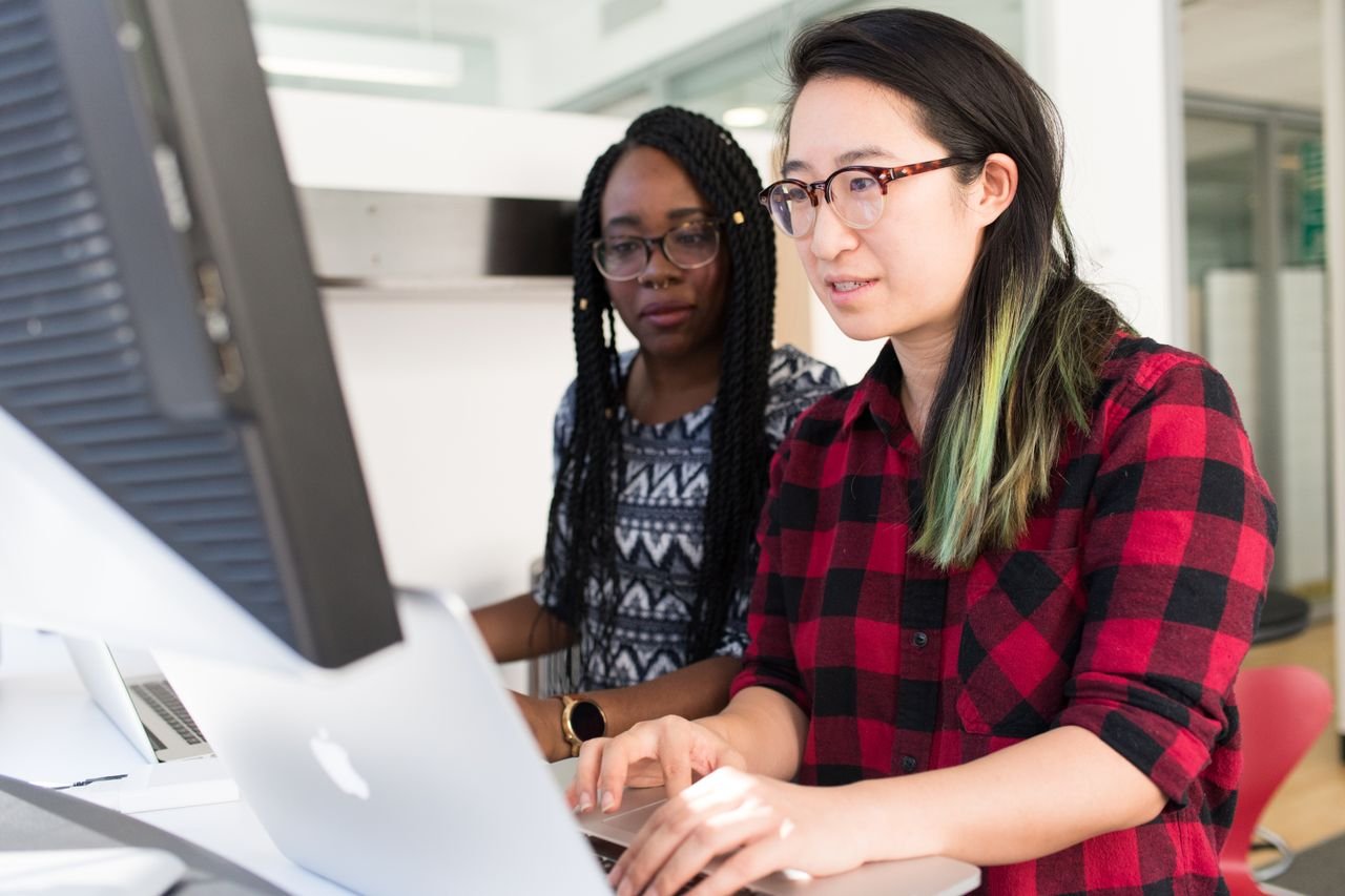 Two developers pairing at a desktop monitor and laptop