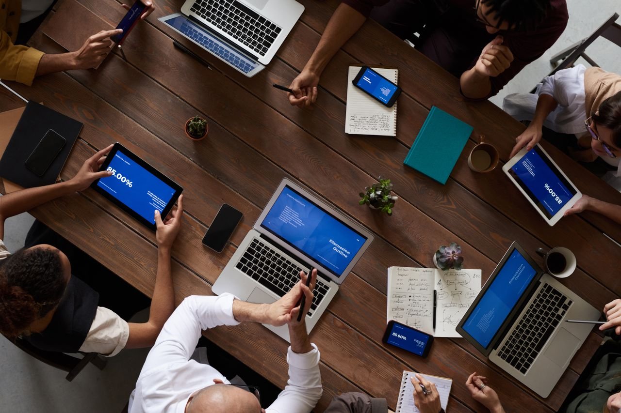 Overhead view of a team meeting with laptops, tablets, and phones showing presentations