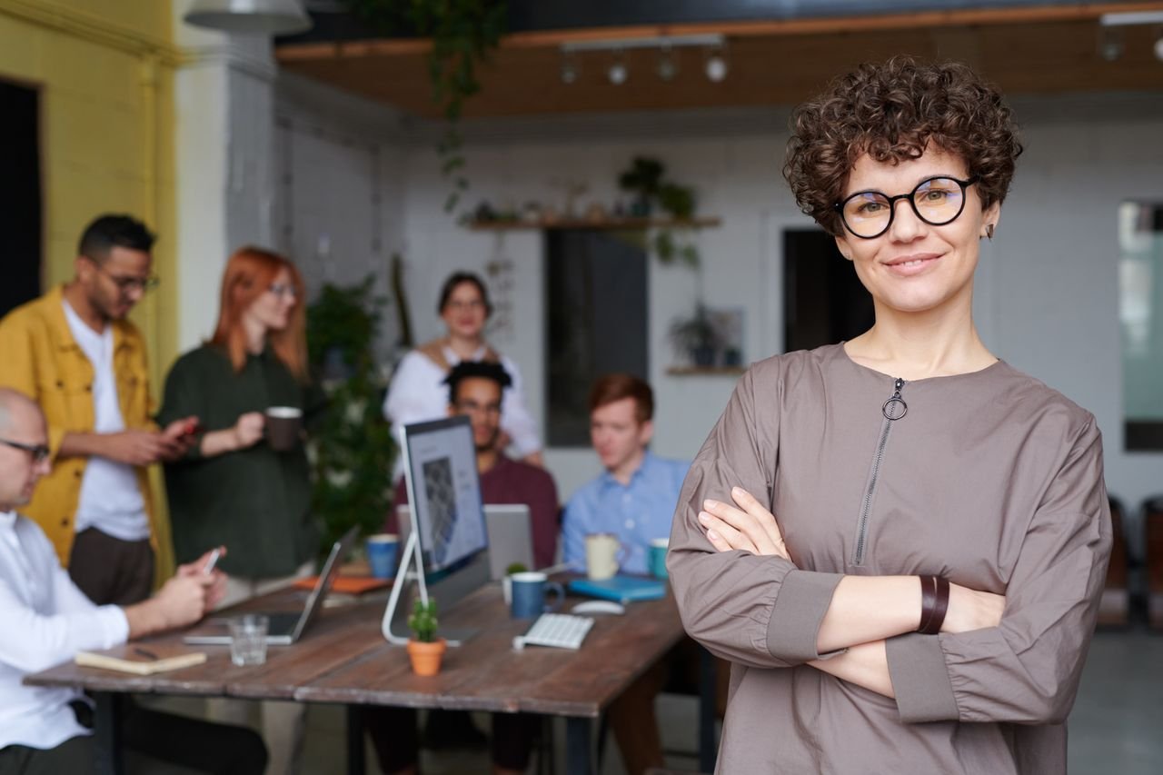 Confident support lead standing with arms crossed while her team works behind her