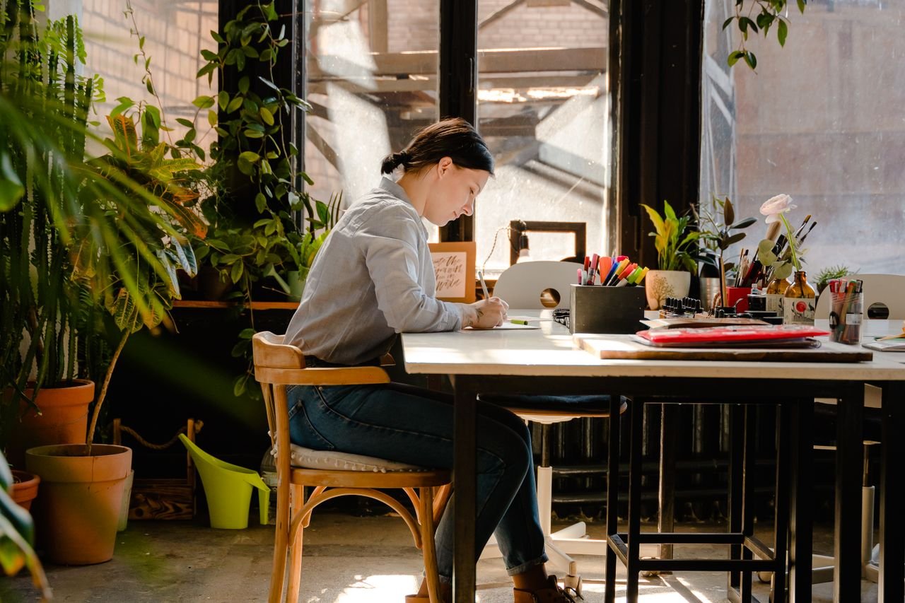 Woman writing notes at a sunny desk surrounded by plants