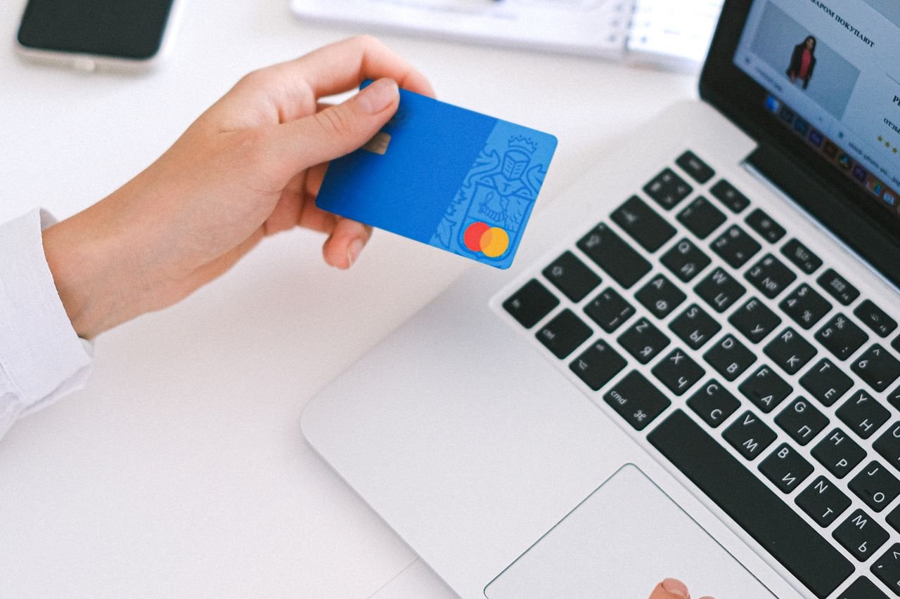 Hand holding a blue credit card next to a laptop during an online checkout