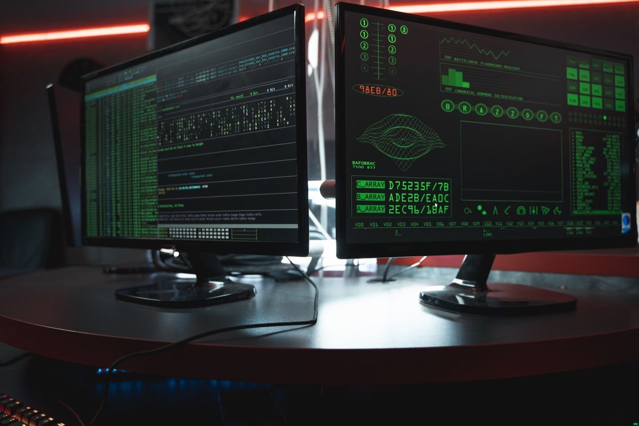 Two monitors displaying green code in a dark room