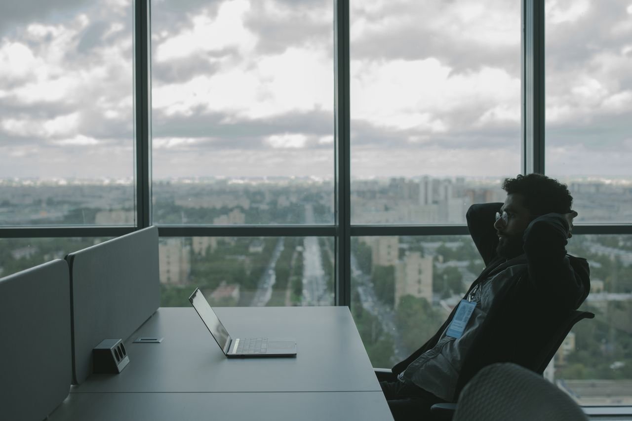Person leaning back at a desk with a laptop and a city skyline view