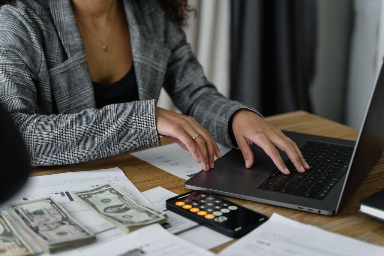 Person reviewing financial charts on a laptop with a calculator and cash