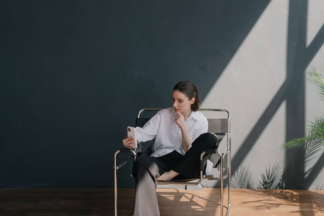 Person sitting in a chair checking a phone in a quiet minimal room